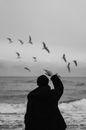 Man in Black Jacket and Black Knit Cap Looking at Birds Flying over the Sea during