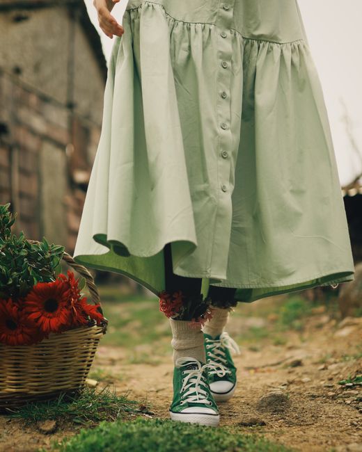 A person in a green dress walking near a flower basket outdoors in Gemlik, Turkey.