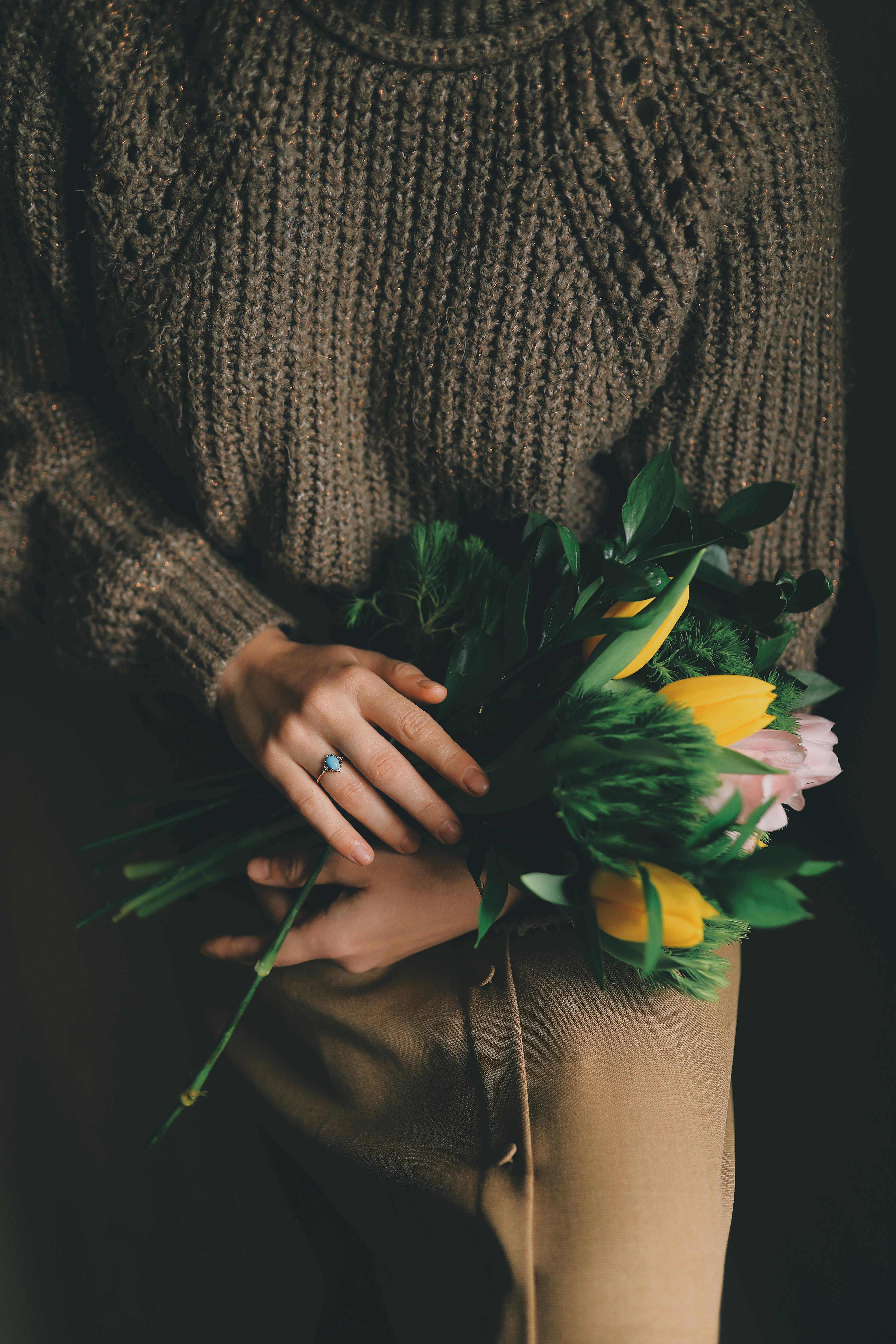 A woman in a knitted sweater holds a vibrant bouquet of tulips, emphasizing warmth and nature.
