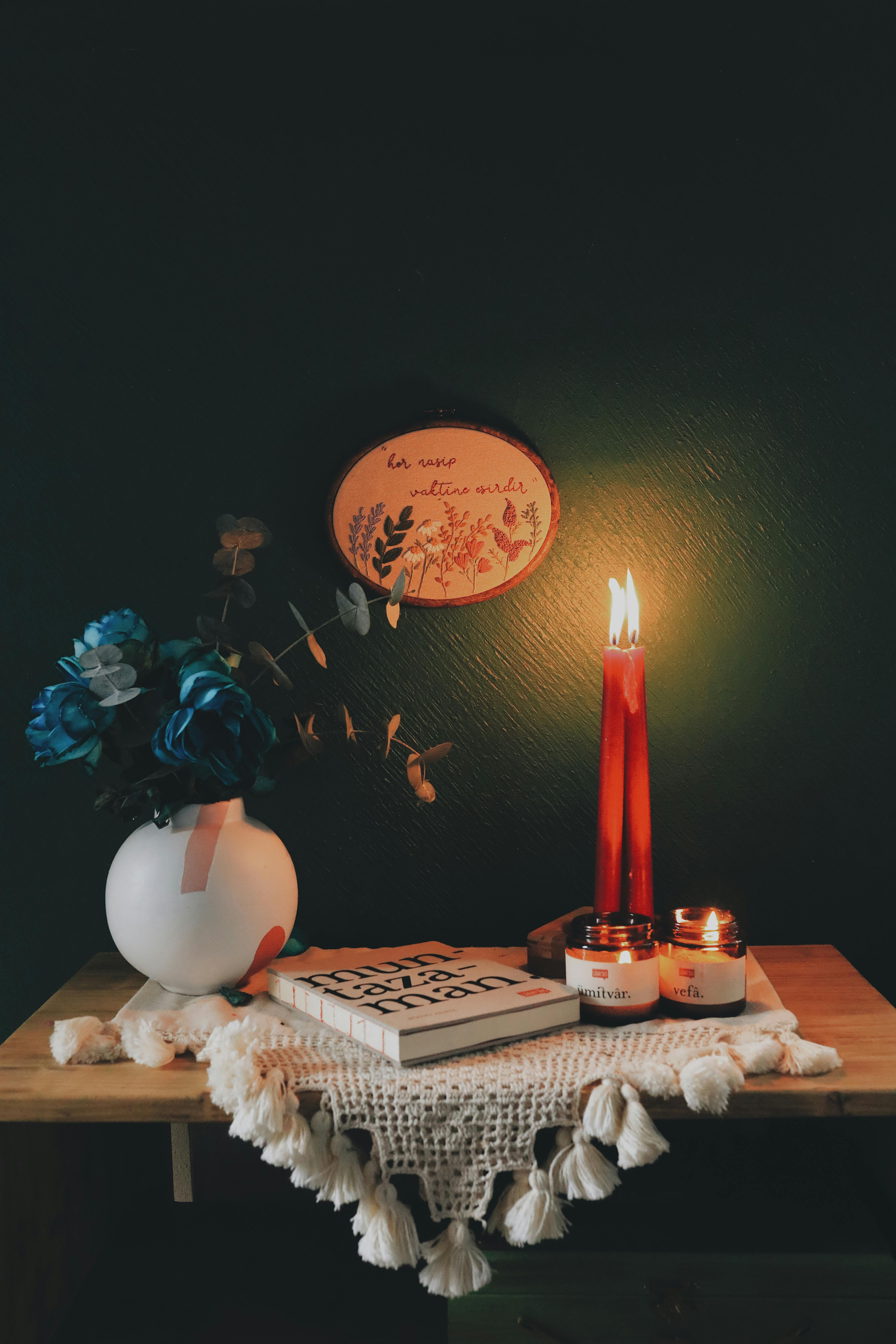 A serene interior setting featuring a candle-lit scene with books and floral decor on a wooden shelf.