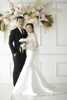 Elegant portrait of Asian bride and groom in wedding attire with floral decor.