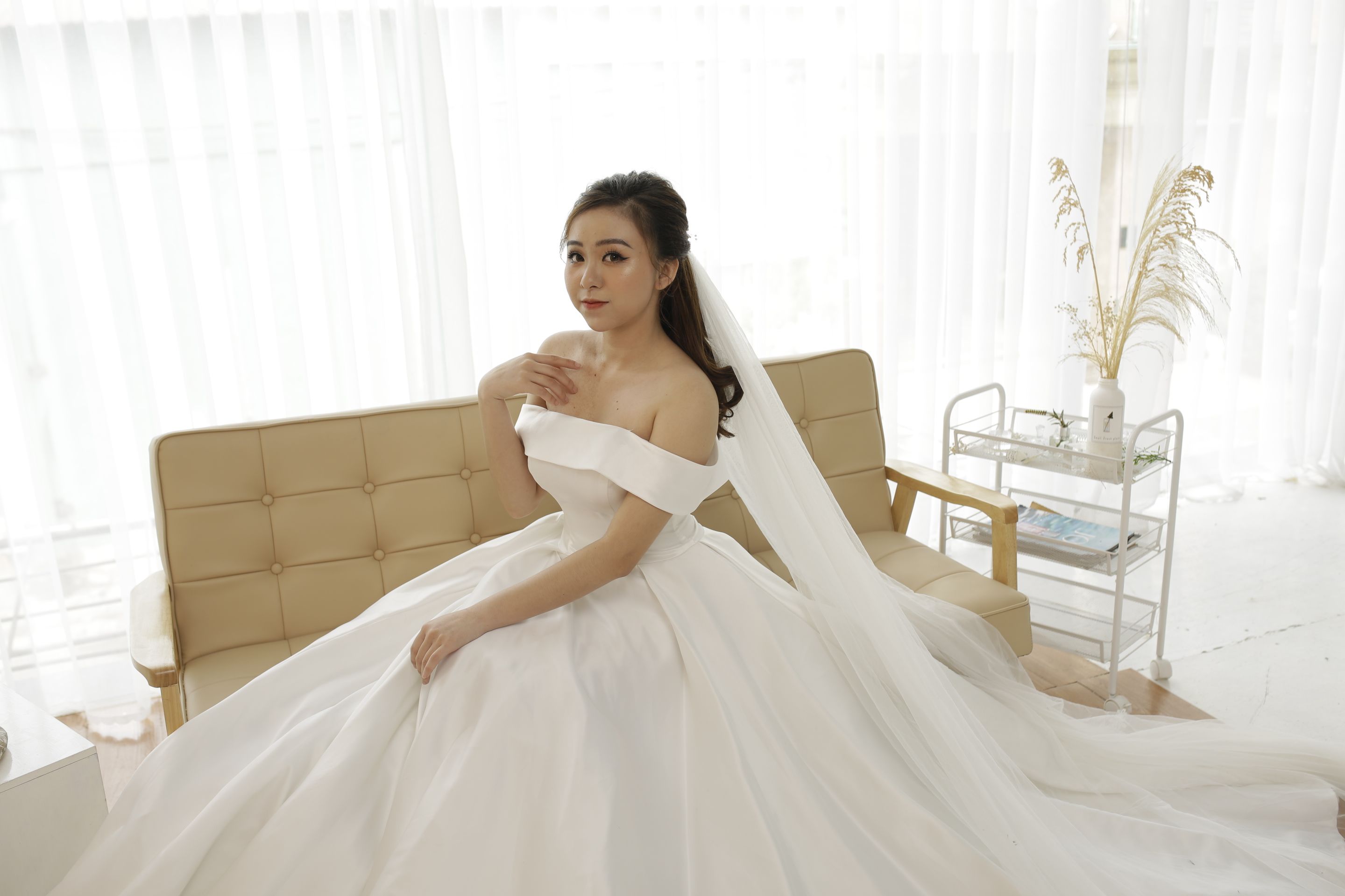 Beautiful Asian bride in an elegant wedding dress posing indoors with a graceful smile.