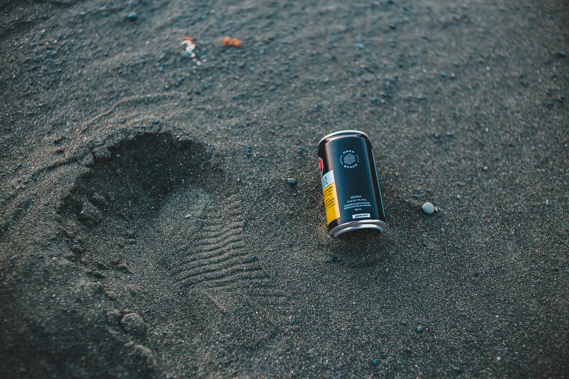 Footprint and can on sand highlight beach pollution and environmental issues.