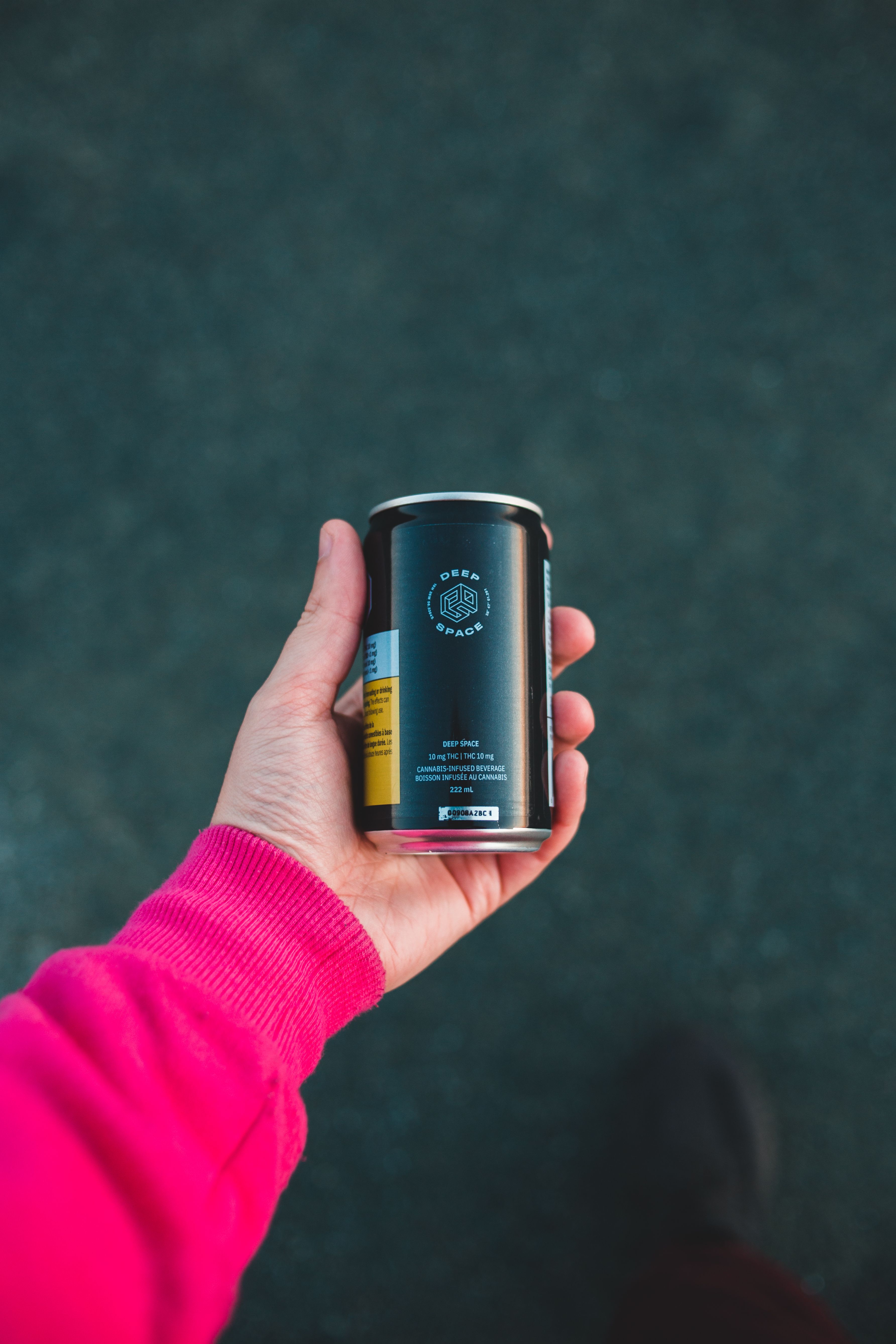 A vibrant image capturing a hand in a pink sleeve holding a black can outdoors.