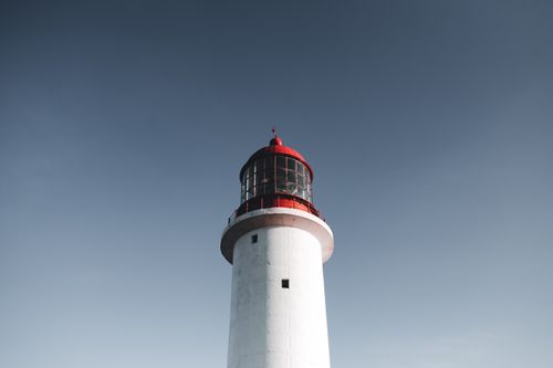 Free Beautiful white lighthouse with a red top tower set against a clear blue sky, captured in daylight. Stock Photo