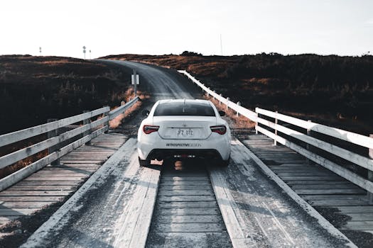 A white car on a scenic wooden bridge road at sunset, perfect for travel and adventure themes.
