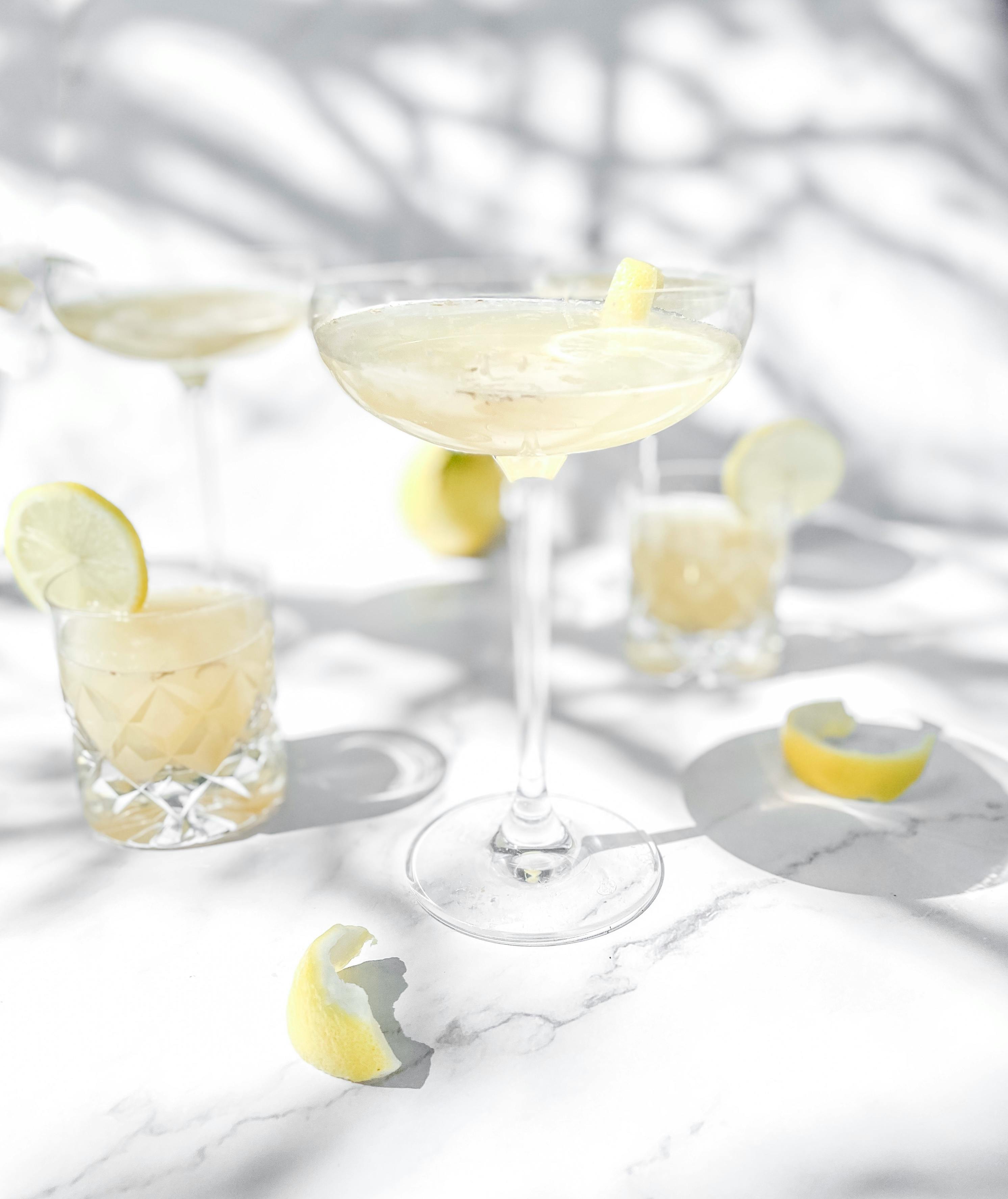Bright lemon cocktail in glass on white background with sunlight shadows, perfect for a refreshing drink concept.