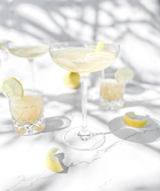 Bright lemon cocktail in glass on white background with sunlight shadows, perfect for a refreshing drink concept.