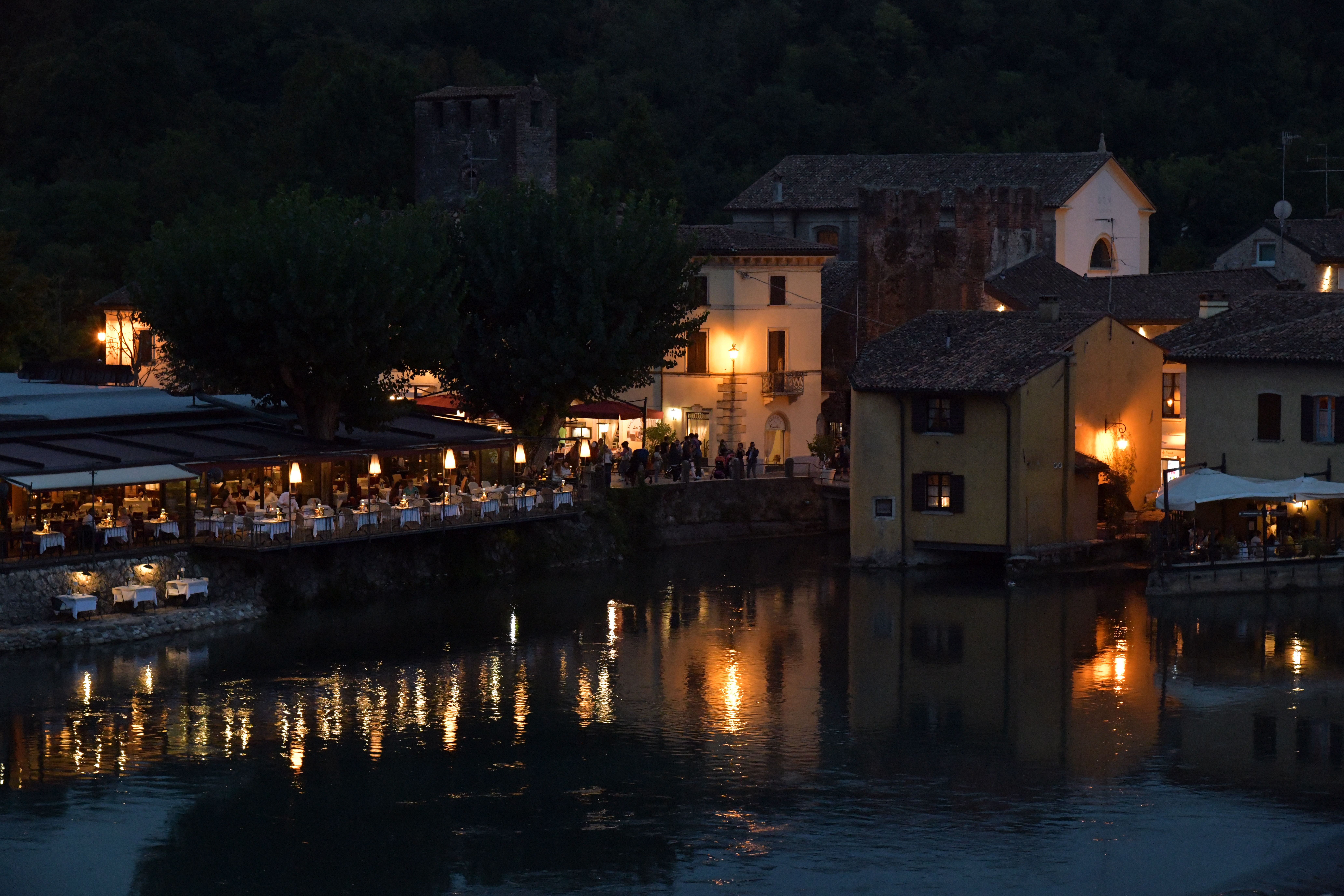 Illuminated waterfront restaurants and reflections at dusk in Borghetto, Veneto, Italy.