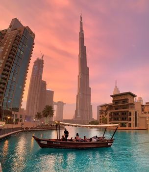 Iconic Burj Khalifa and boat on Dubai canal at sunset, showcasing city skyline.