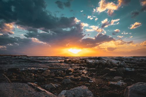 Free Stunning sunset view with dramatic clouds over a rocky seashore in Van, Türkiye. Vibrant colors and serene waves. Stock Photo