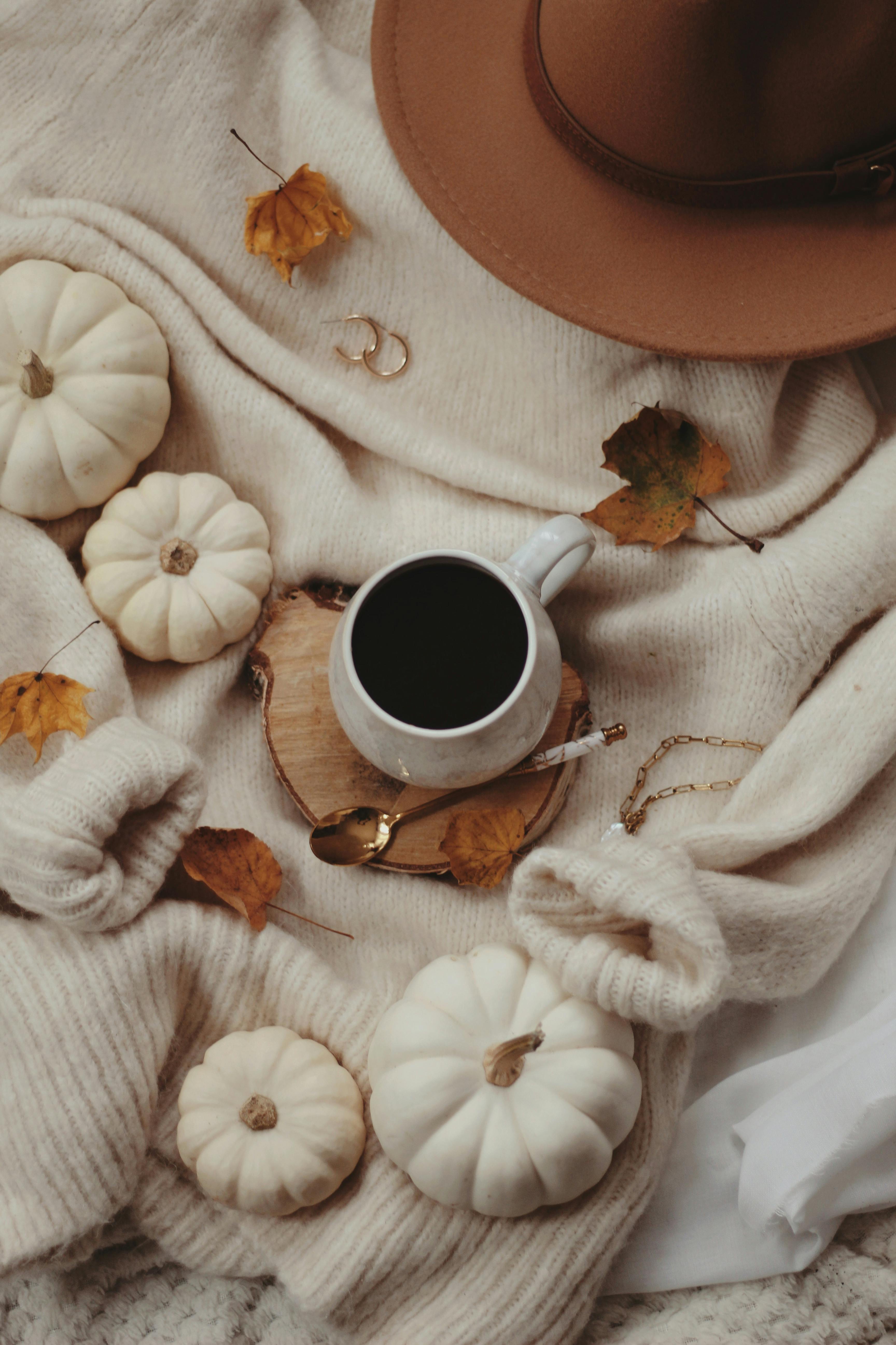 Warm autumn still life with a ceramic cup of coffee, pumpkins, and cozy knitwear.