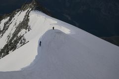 Two climbers ascend a snow-covered mountain ridge, showcasing adventure in a winter landscape.