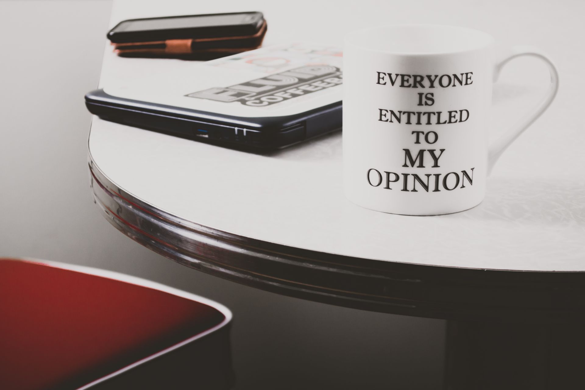 A coffee mug with a humorous quote on a desk alongside a laptop, smartphone, and notepad.