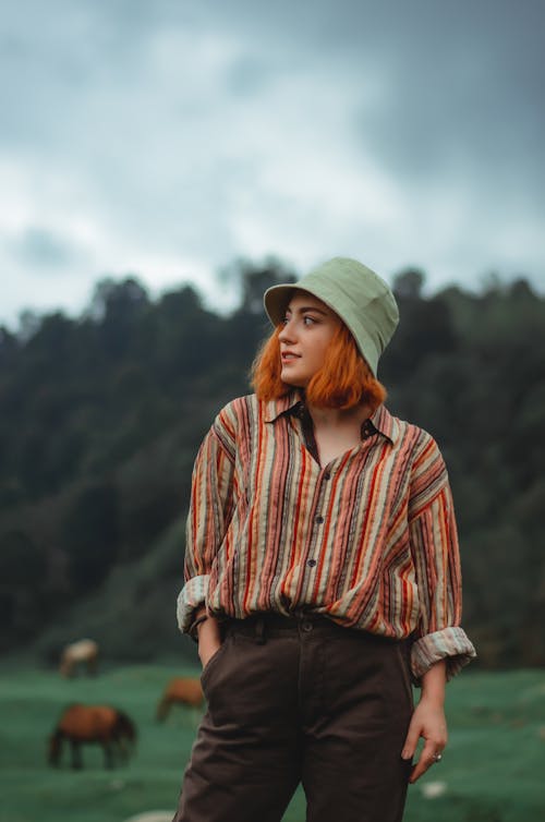Woman in Brown and White Striped Long Sleeve Shirt and Gray Hat Standing on Green Grass