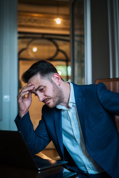 Free A worried businessman in a blue suit working on his laptop in an office environment. Stock Photo