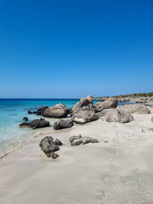Free Tranquil beach scene featuring rocks, clear water, and vivid blue sky. Stock Photo