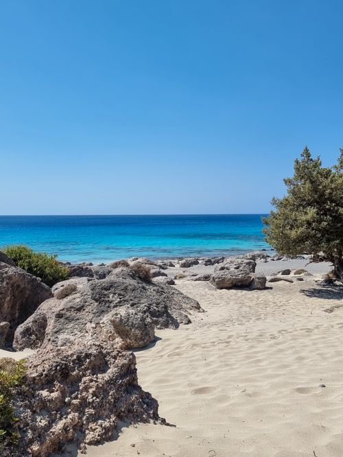 Free Beautiful sandy beach with turquoise water, rocky shoreline, and clear blue sky. Perfect summer getaway. Stock Photo