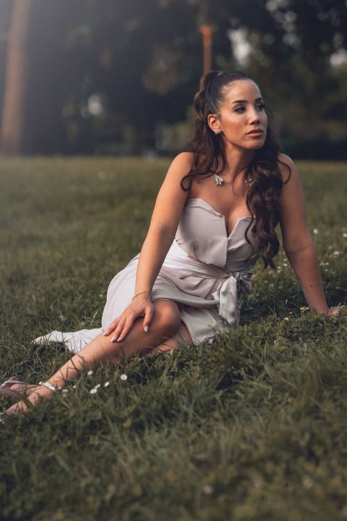 Free A woman in a dress elegantly sits on a grassy field, creating a serene and elegant atmosphere. Stock Photo