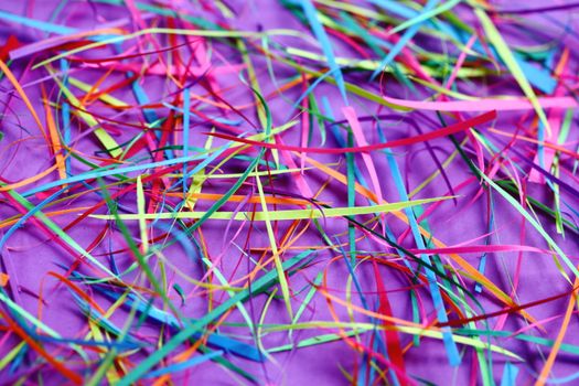 Bright and colorful paper shreds scattered on a purple surface, creating a vivid abstract pattern.