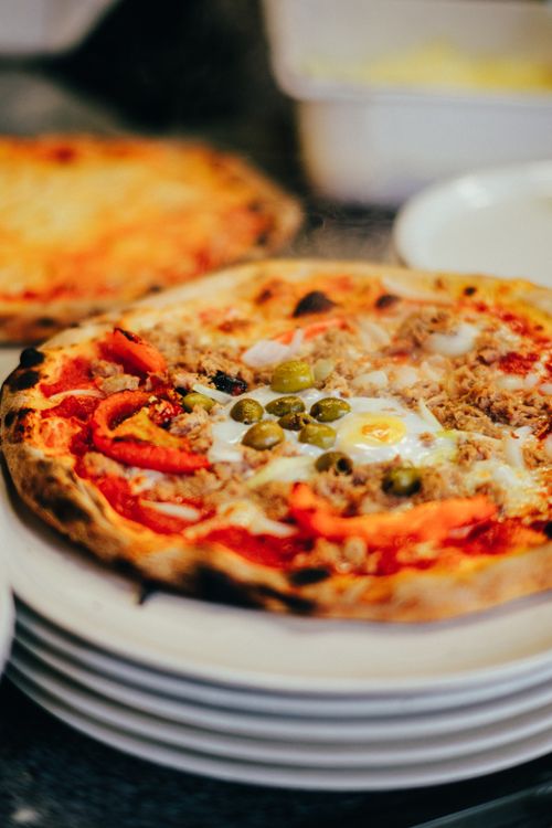 Free Close-up of a freshly baked pizza topped with green olives, red peppers, and eggs, served hot. Stock Photo