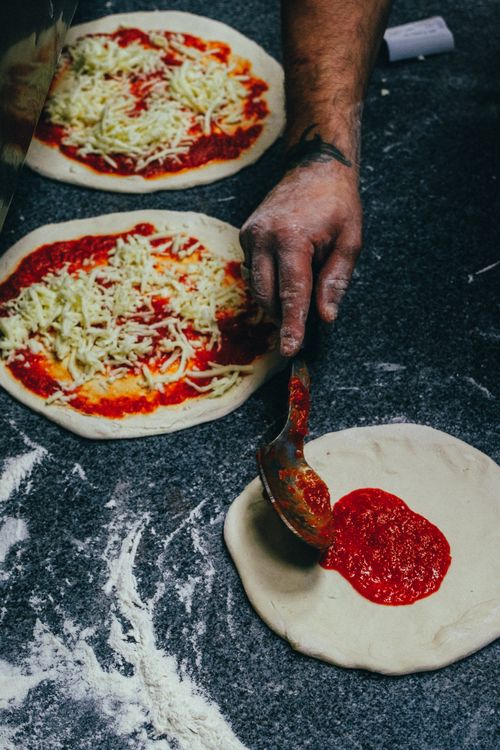 Free Close-up of a chef's hand spreading tomato sauce on pizza dough in a kitchen. Stock Photo