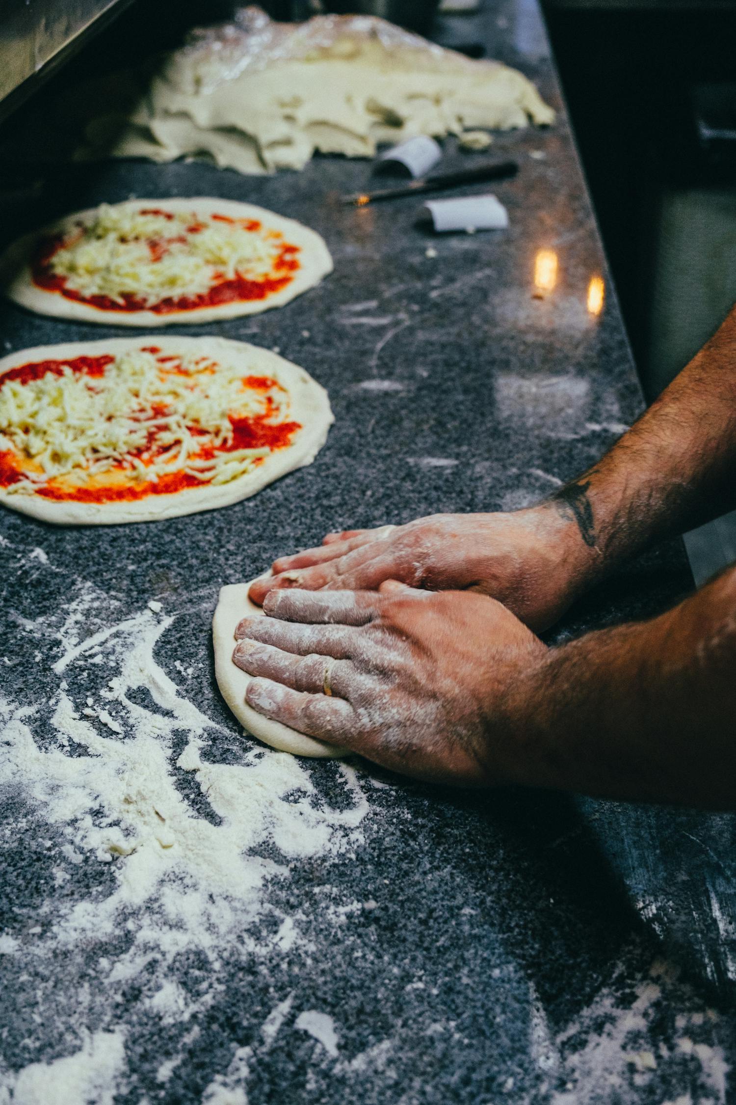 Hands crafting pizza dough with flour on a marble countertop