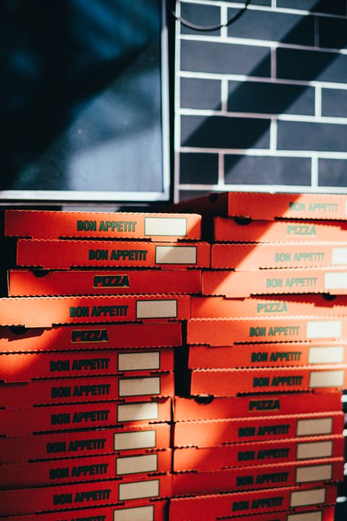 Free A vertical stack of orange pizza boxes illuminated by sunlight indoors. Stock Photo
