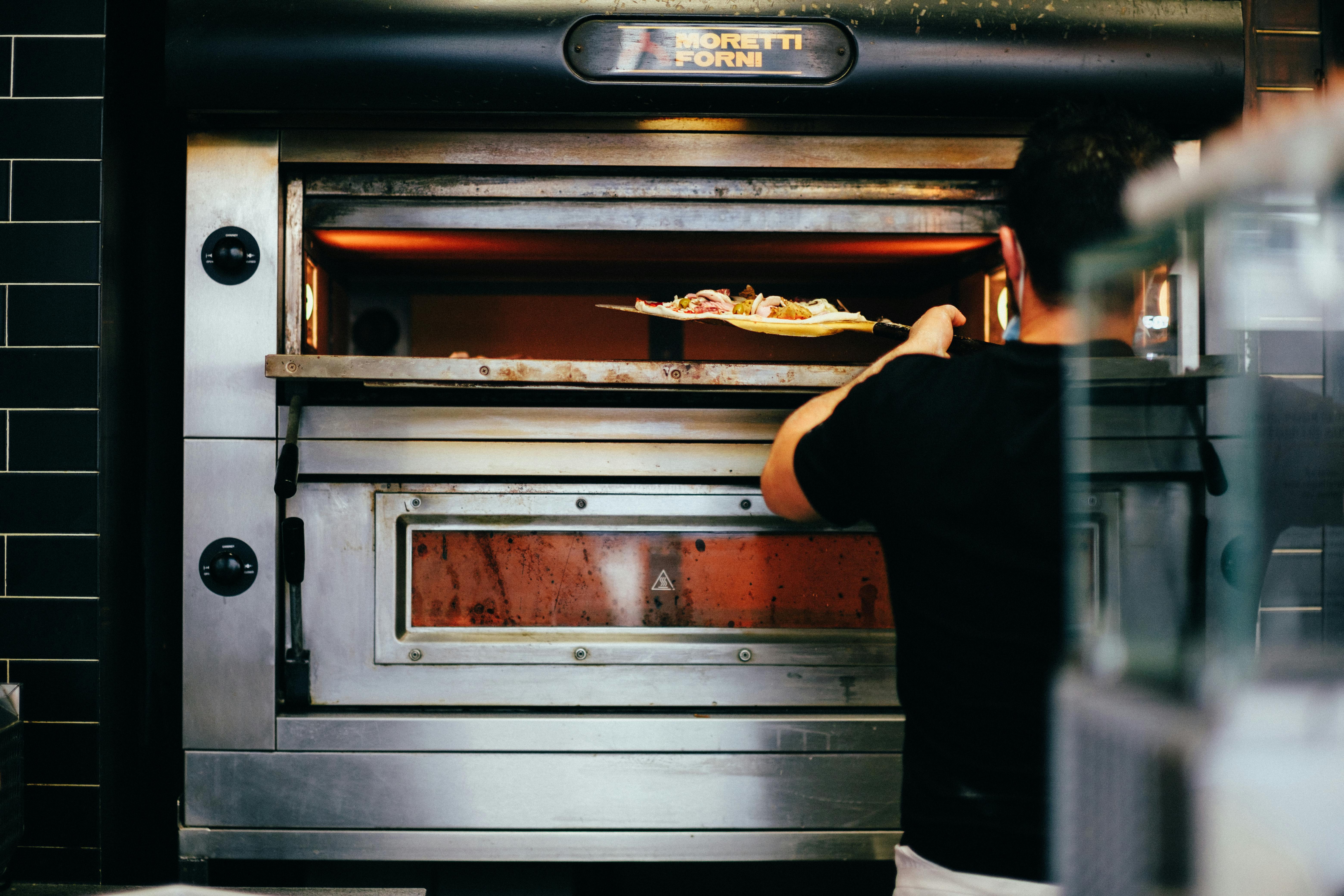Professional chef placing a freshly prepared pizza into a high-temperature industrial oven.