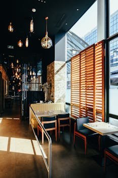 Sunlit modern restaurant interior featuring stylish chairs, tables, and hanging lights.