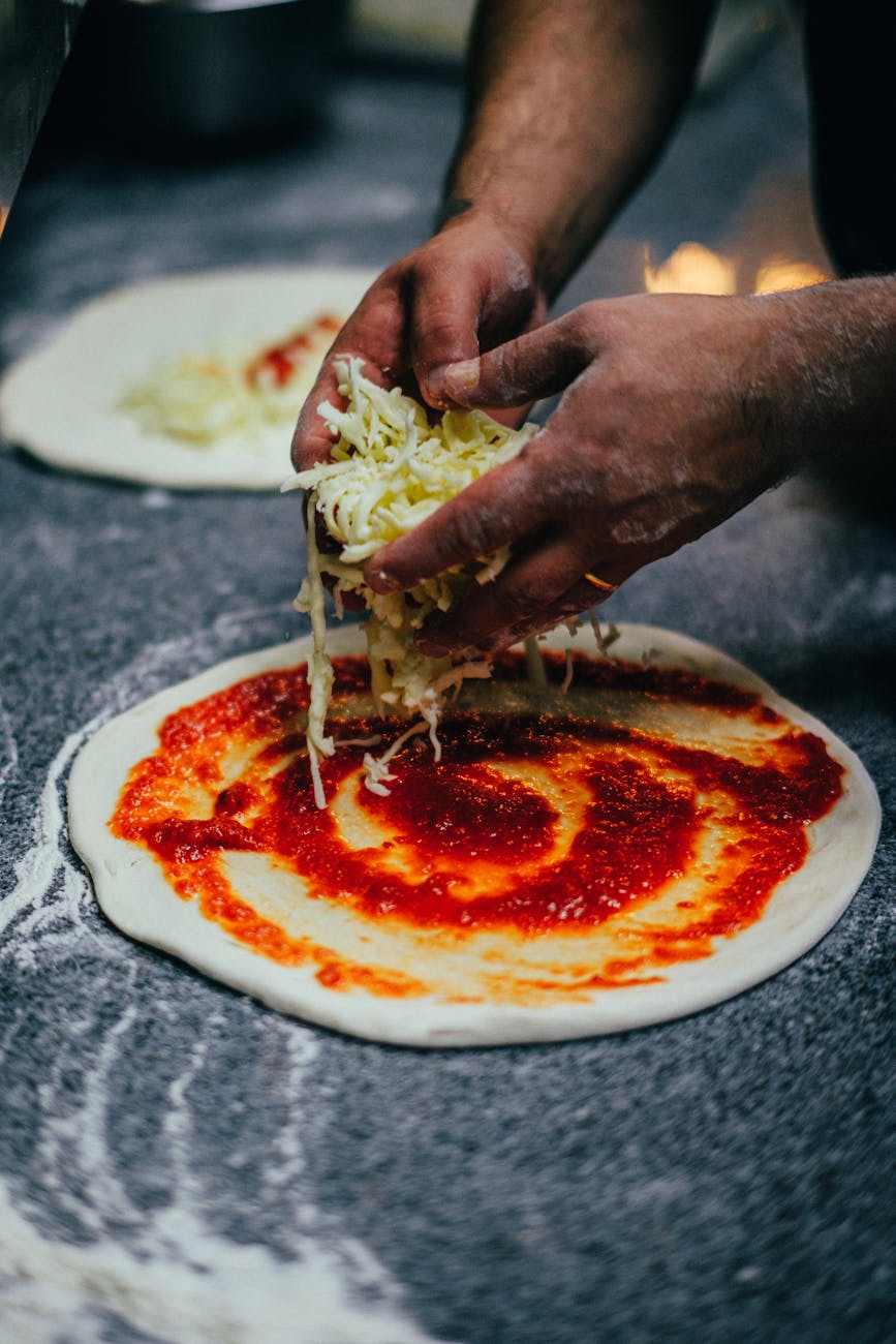 Close-up of a chef adding cheese to pizza dough with tomato sauce.