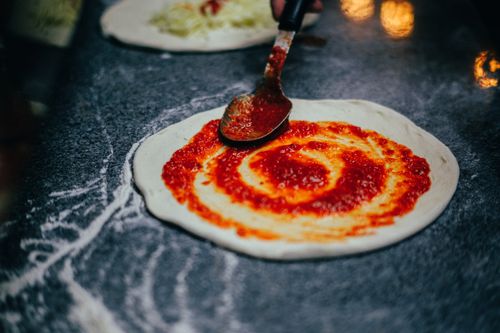 Free Preparing pizza dough with tomato sauce using a spoon in a kitchen setting. Stock Photo