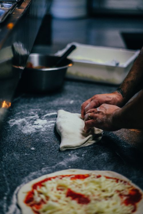 Free Hands folding dough with cheese pizza in foreground in a professional kitchen. Stock Photo