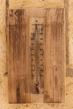 A close-up of an aged wooden thermometer mounted on a brick wall showing temperature in Celsius.
