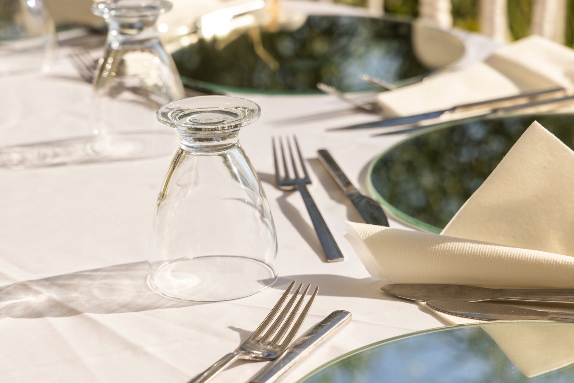 A stylish outdoor table setting with glassware, cutlery, and napkins on a sunny day.