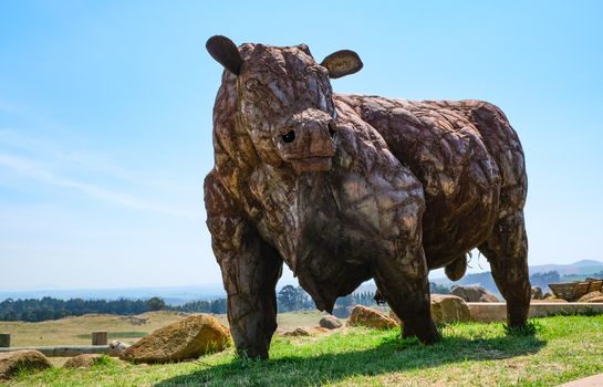 A striking bull sculpture stands proudly in a vast rural field under a clear blue sky.