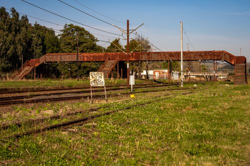 Free A neglected rusty footbridge spanning abandoned railway tracks in a quiet rural setting. Stock Photo