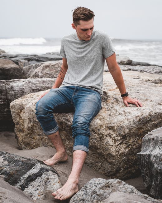 Man sitting on rocks at the beach, enjoying a serene seaside moment.