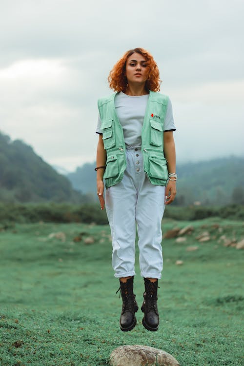 Woman in Green Button Up Shirt and White Pants Standing on Green Grass Field