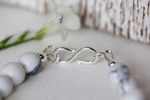 A delicate silver clasp on a beaded necklace, accentuated by a floral backdrop.