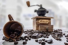 Wooden coffee grinder with beans and chocolate on a rustic table setting.