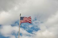 The United States flag waving on a tall flagpole under a cloudy sky.