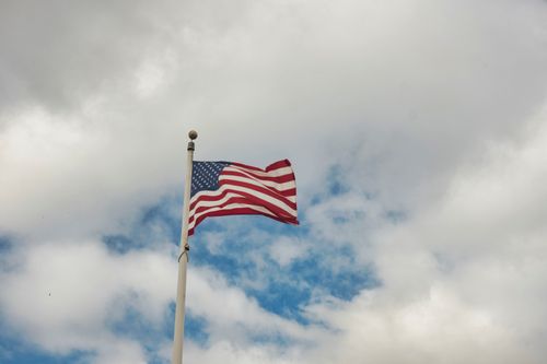 Free The United States flag waving on a tall flagpole under a cloudy sky. Stock Photo