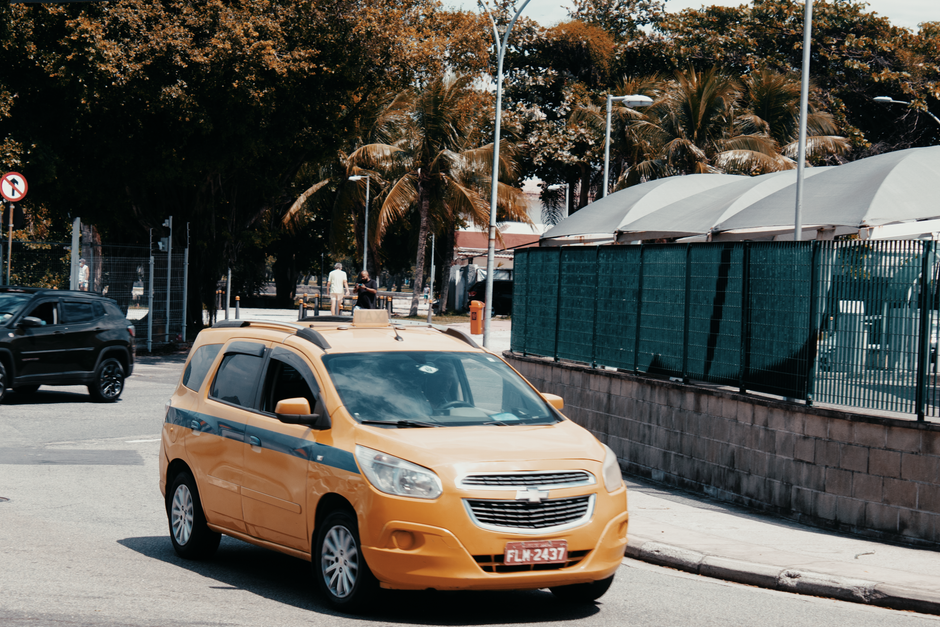 A yellow taxi drives through the bustling streets of Rio de Janeiro, Brazil, under sunny skies.