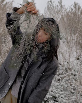 Asian woman in winter clothing holding tree branch in snowy landscape.