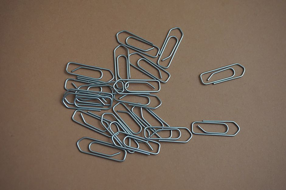 A collection of metal paper clips scattered on a brown surface, showcasing office supplies.
