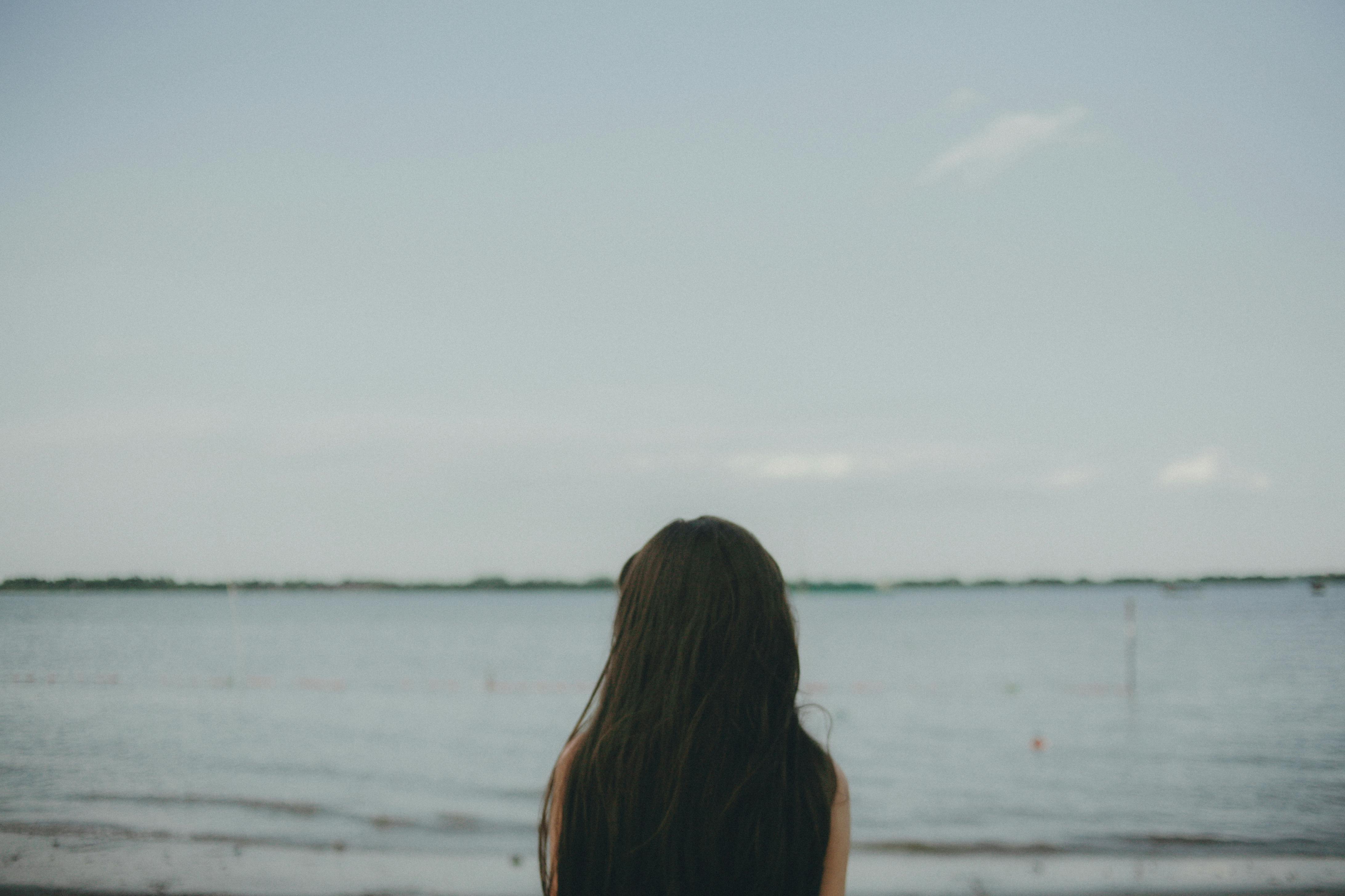 Woman with long hair facing the calm beach, evoking a sense of solitude and peace.