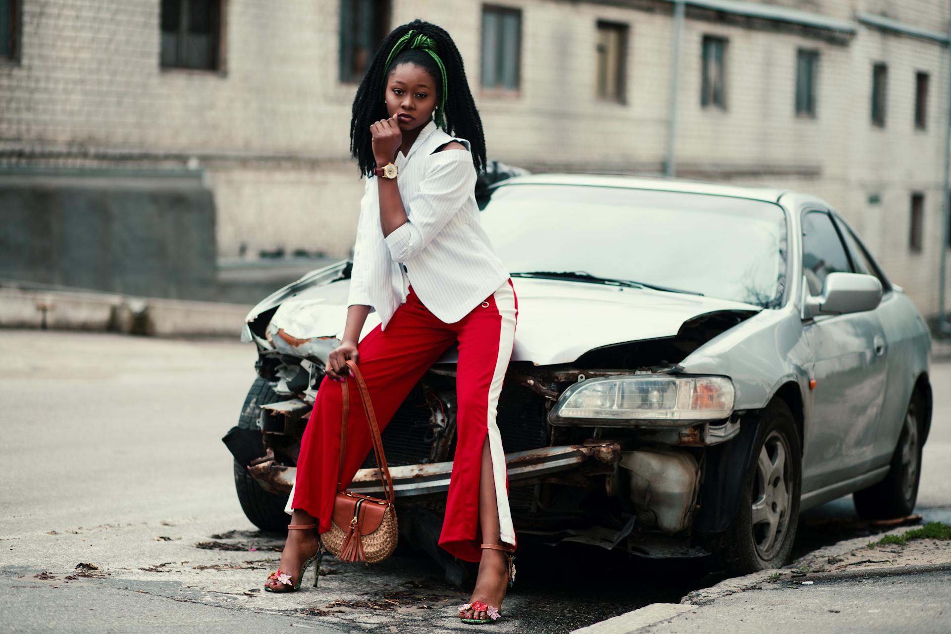 Stylish woman in city street, posing beside a damaged car. Fashion meets urban decay.