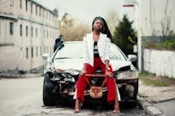 一名时尚女子自信地在城市环境中，于一辆受损的汽车上摆出姿势