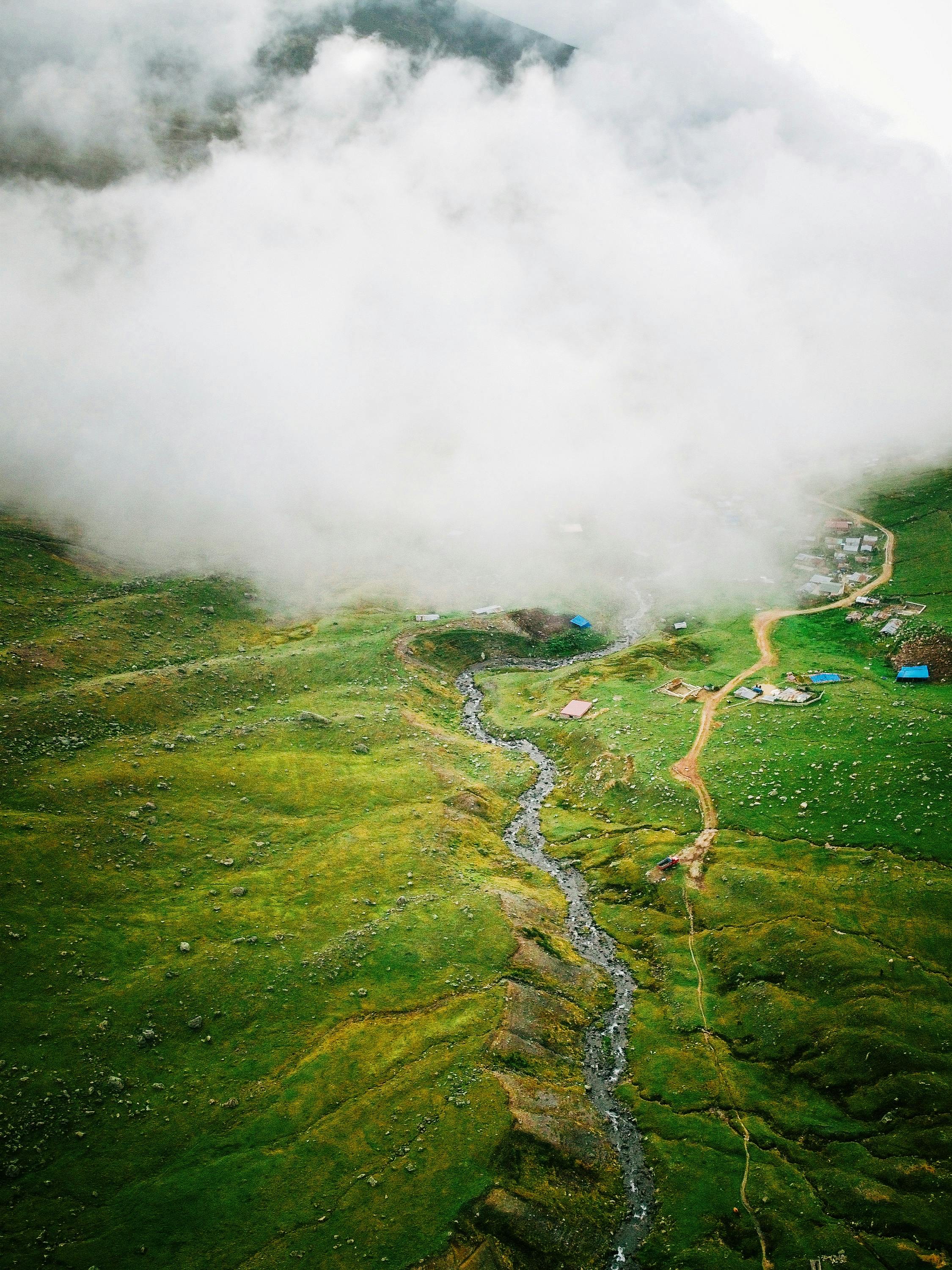 Dramatic aerial shot showcasing a lush green landscape with a winding stream, shrouded in fog.